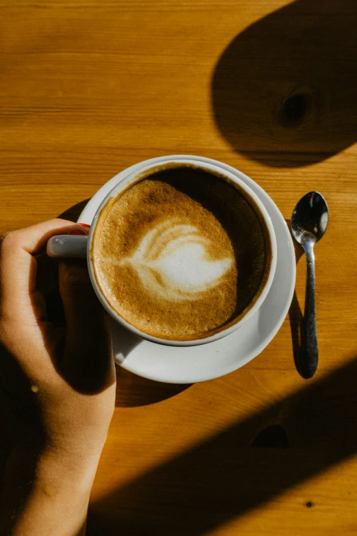 a hand holding a cup of coffee on top of a wooden table