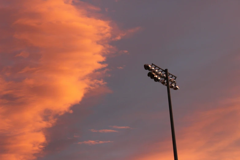 a tall metal street light in front of a pink sky