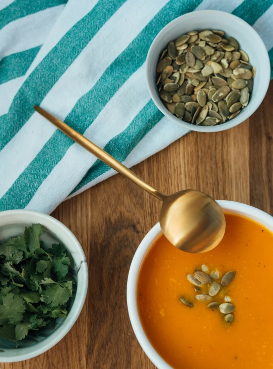 bowls of soup, carrots, and spinach with a spoon