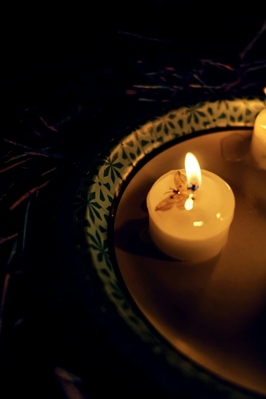 two small candles sit on a dish, with the first lit in the dark