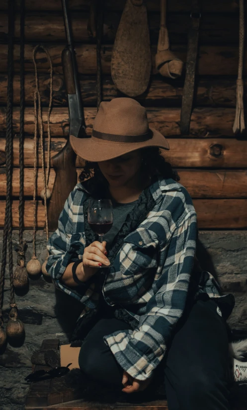 a woman with a plaid shirt and a hat is holding a glass of wine