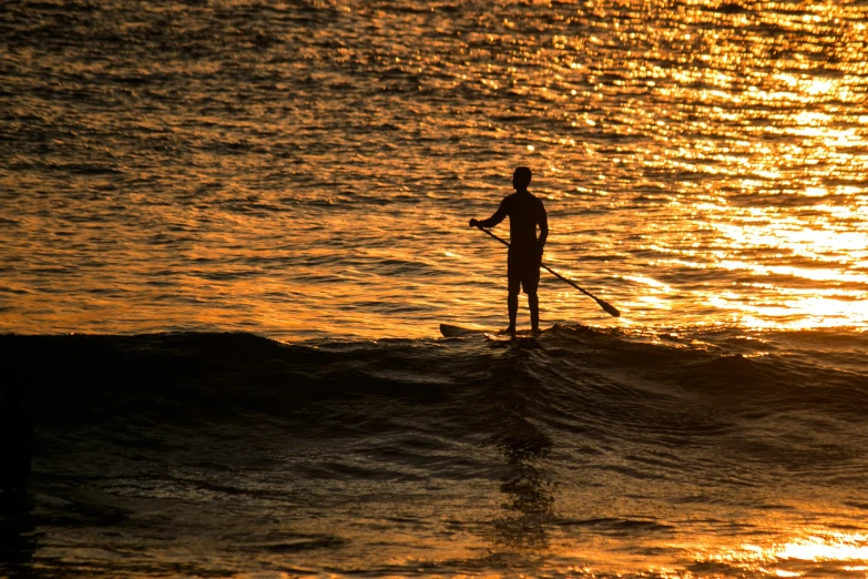 man standing on surfboard in ocean at sunset