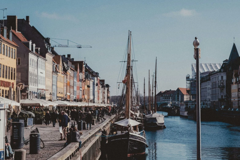 boats parked in the water near buildings and people walking on the shore