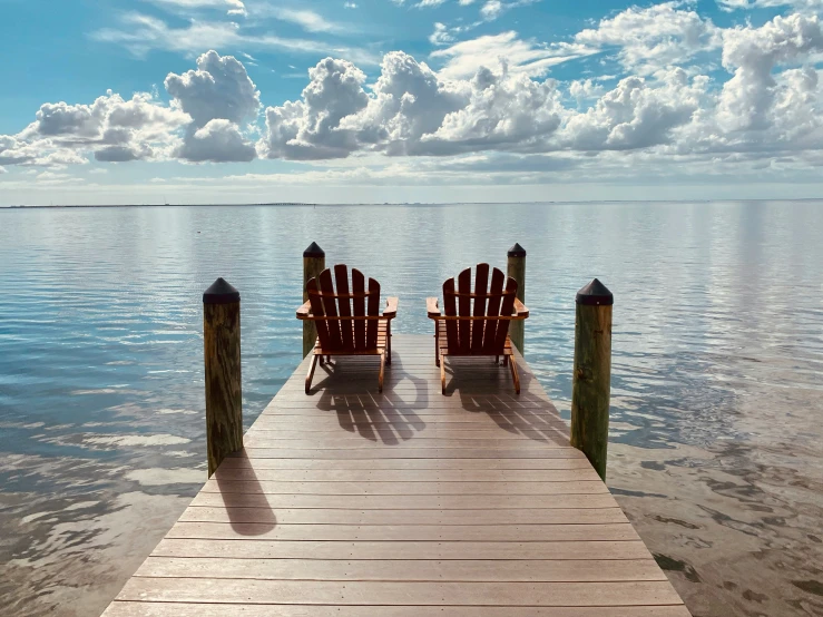 two empty chairs sitting on top of a wooden dock