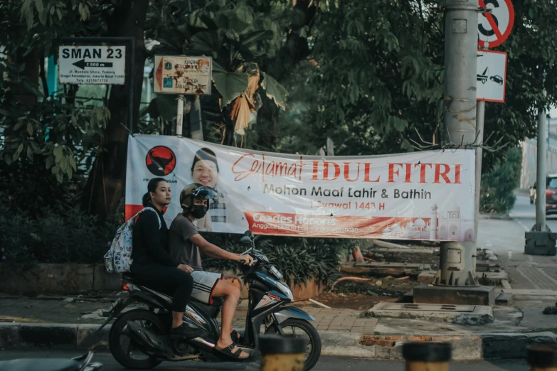 two men are sitting on a motorcycle near a sign