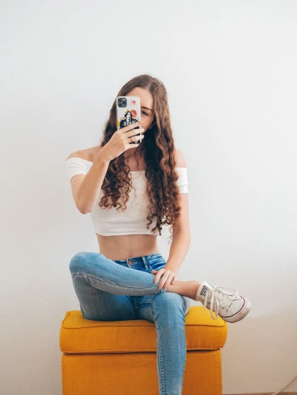 a beautiful young woman sitting on top of a yellow bench taking a selfie