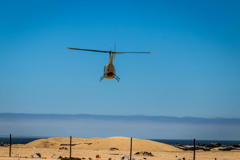 helicopter flying low to the ground with people on the beach behind it