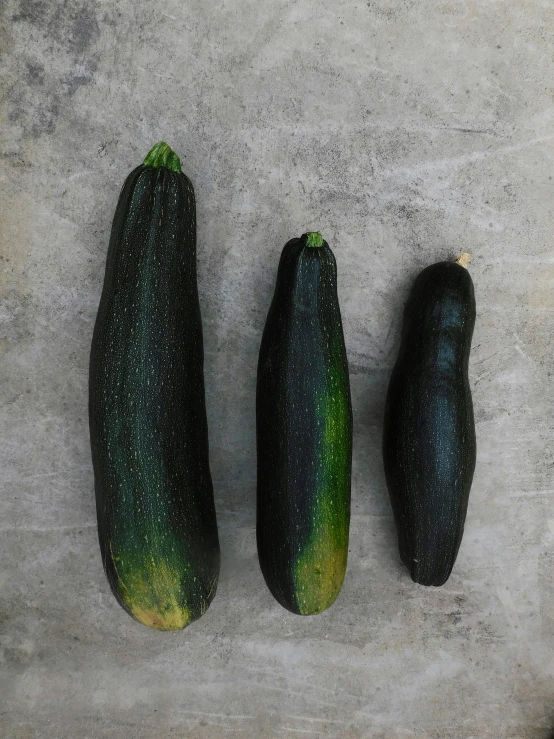 three fresh - looking cucumbers sit on a concrete surface