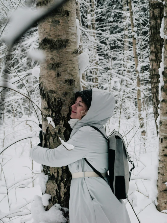 a woman in a hooded jacket is leaning against a tree in the snow