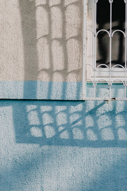 sunlight coming through the window casts a long shadow on a blue wall