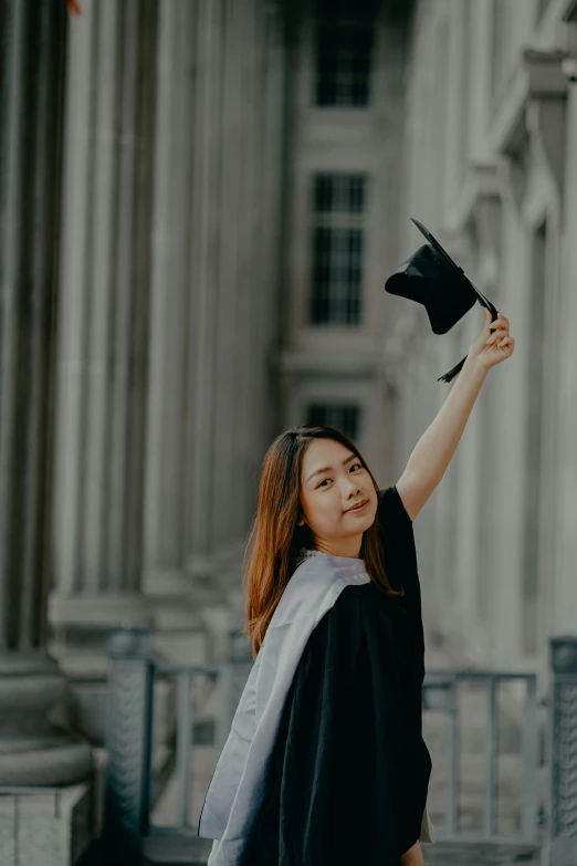 a woman in a graduation gown and mortar on her shoulder stands outside an university building