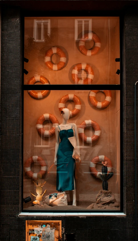 a mannequin dressed in a dress looks at donuts on display behind the glass