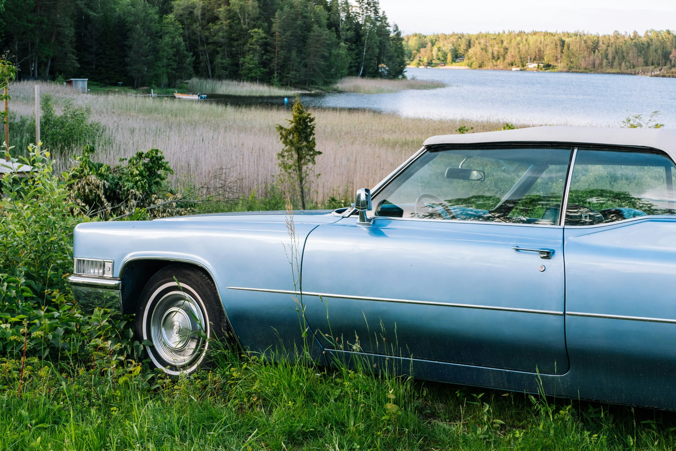 the blue convertible has been parked by a lake