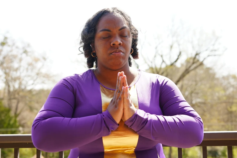 woman wearing purple holding her hands together in the air while standing outside