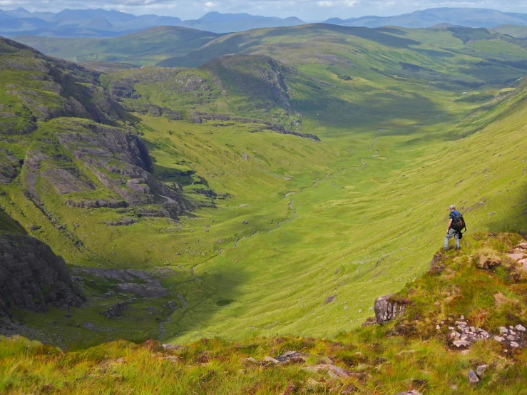 the hiker is standing on a grassy slope above a valley