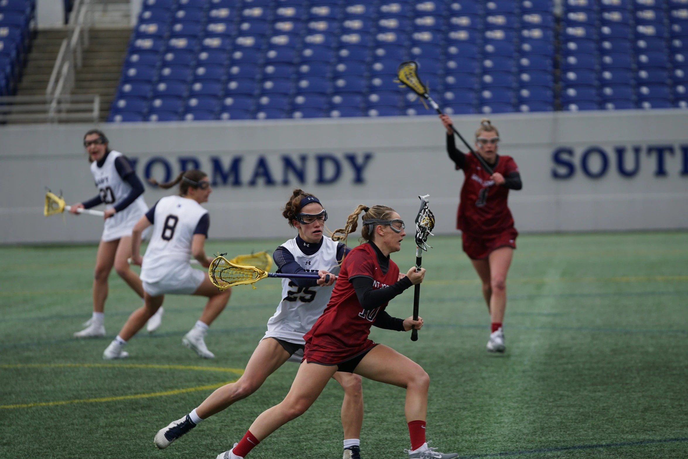 girls playing lacrosse on an indoor field in front of a crowd