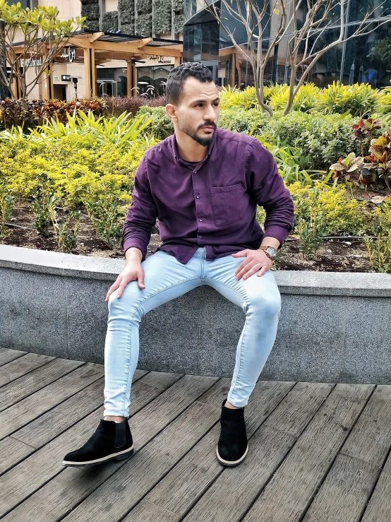 man sitting on cement bench in front of some bushes and plants