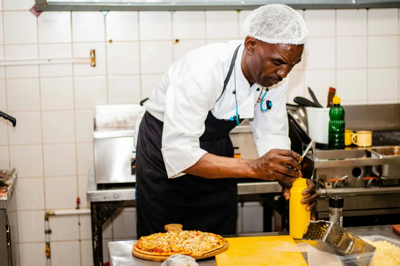 a man in an apron holding a knife near a pizza