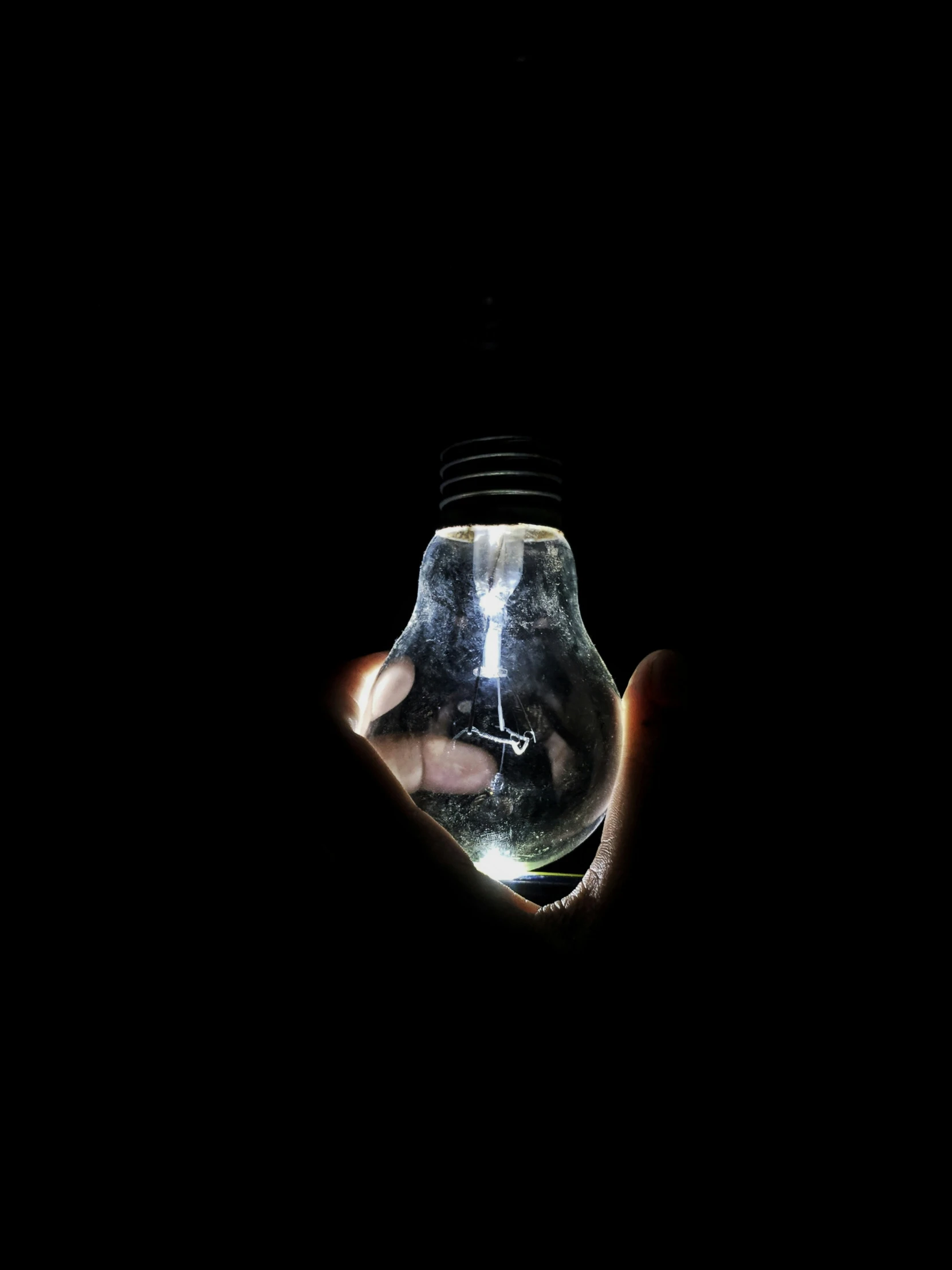 an illuminated light bulb with two hands that are touching each other