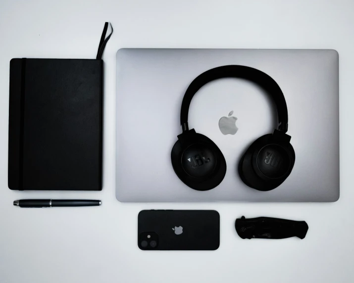 an apple laptop is next to two headphones and a pen