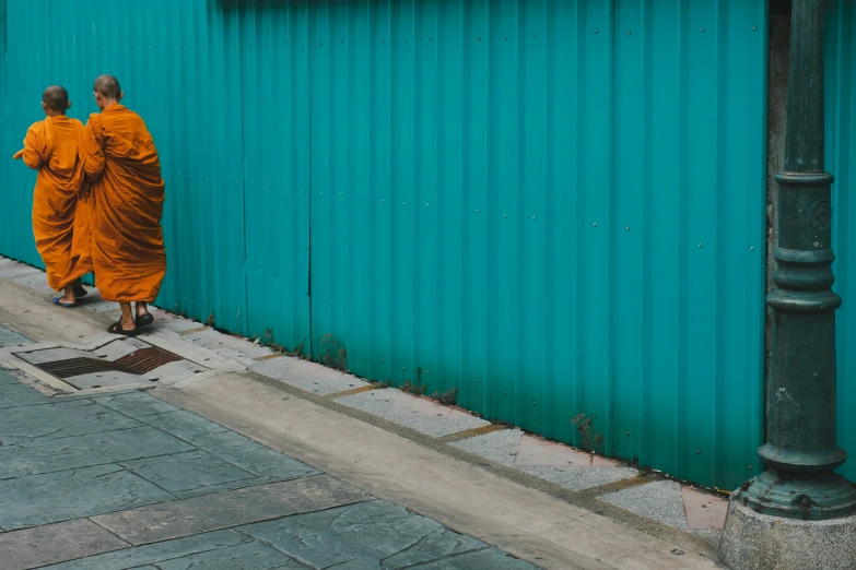 two monks walking down a sidewalk near a blue building