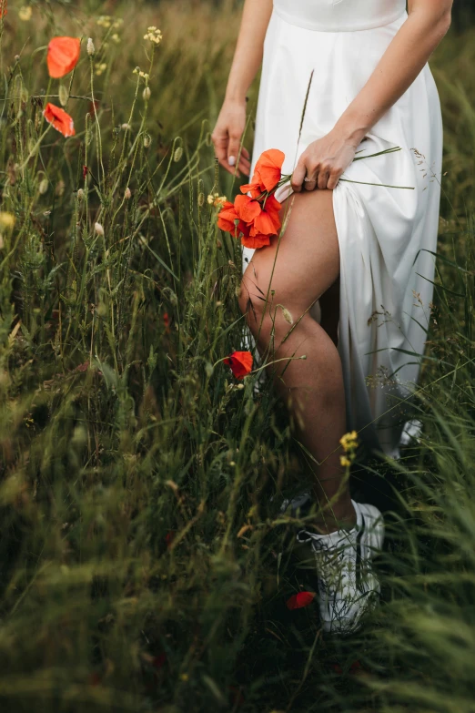 a woman in white shirt and dress kneeling on grass with red flowers