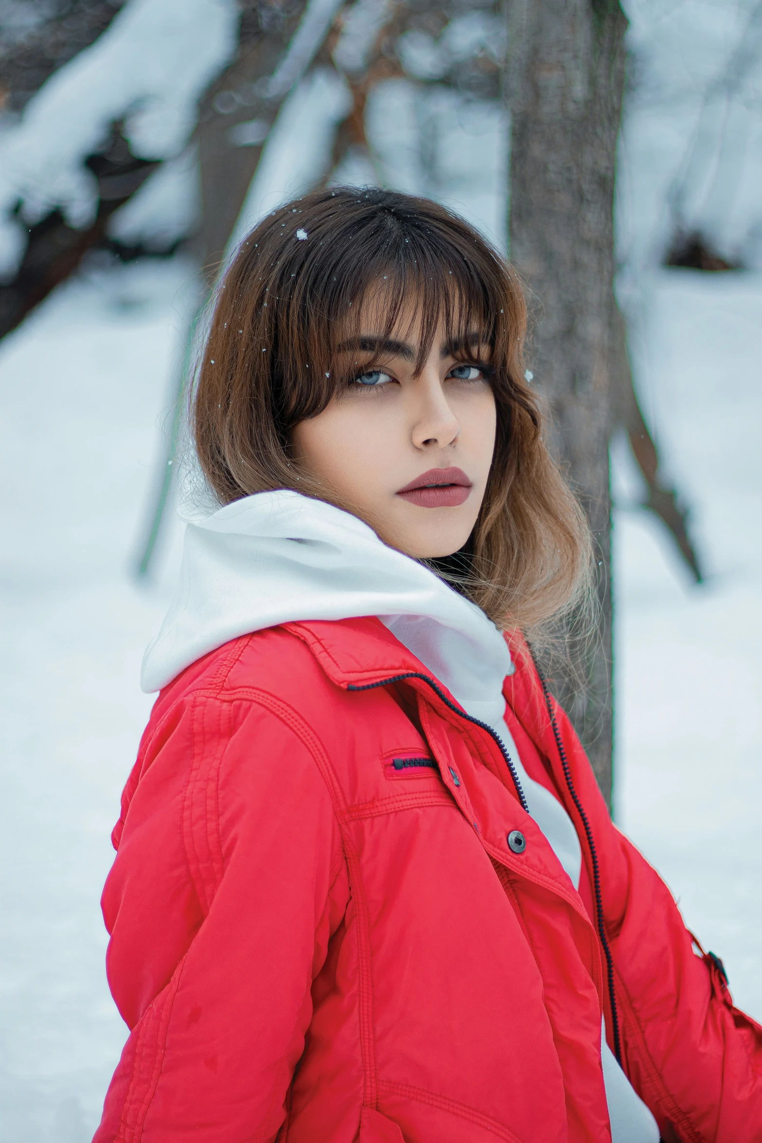 a woman in red standing by a tree wearing winter clothes