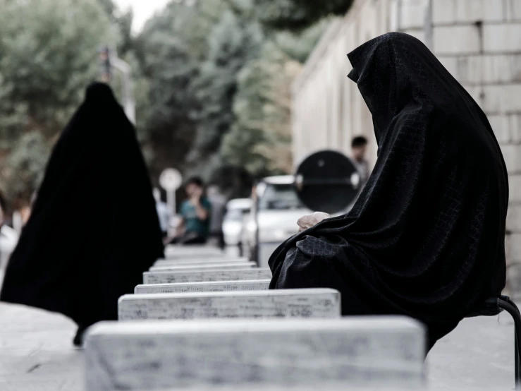 two women wearing black burka sit on benches outside