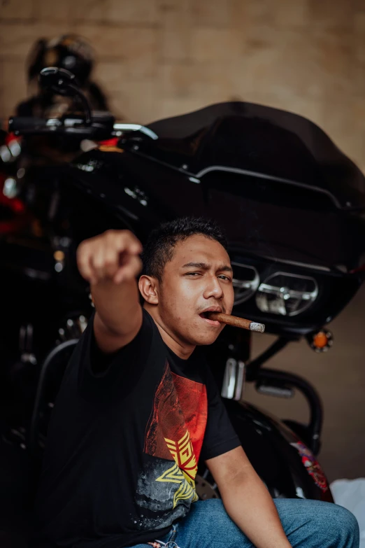 the man smokes a cigarette and is sitting beside his motorcycle