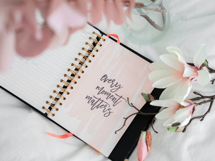 a pink notebook is laying next to flowers