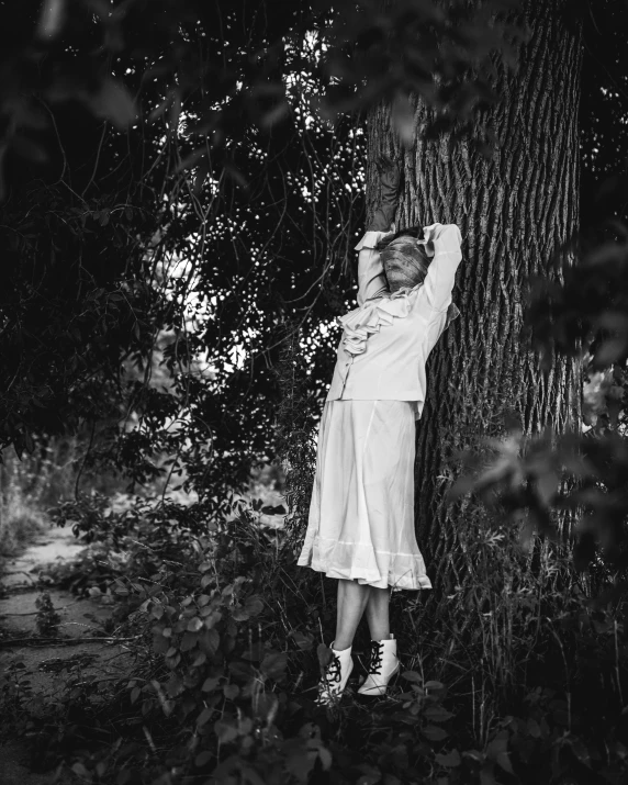 a girl is standing under a tree in the woods