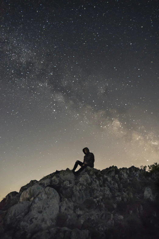 a man sits on top of a rock with the night sky