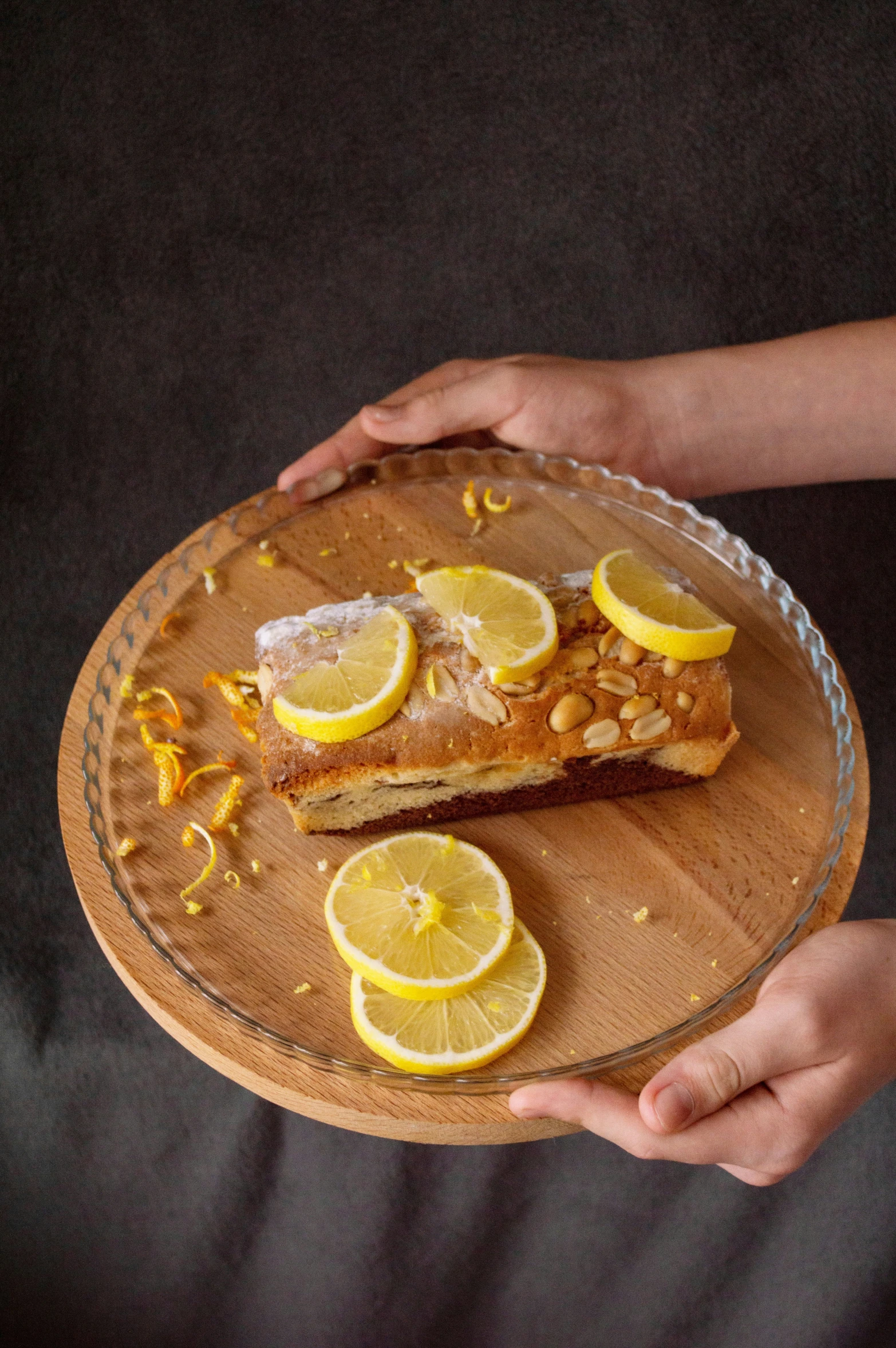 person holding a wooden serving plate of fish and slices of lemon