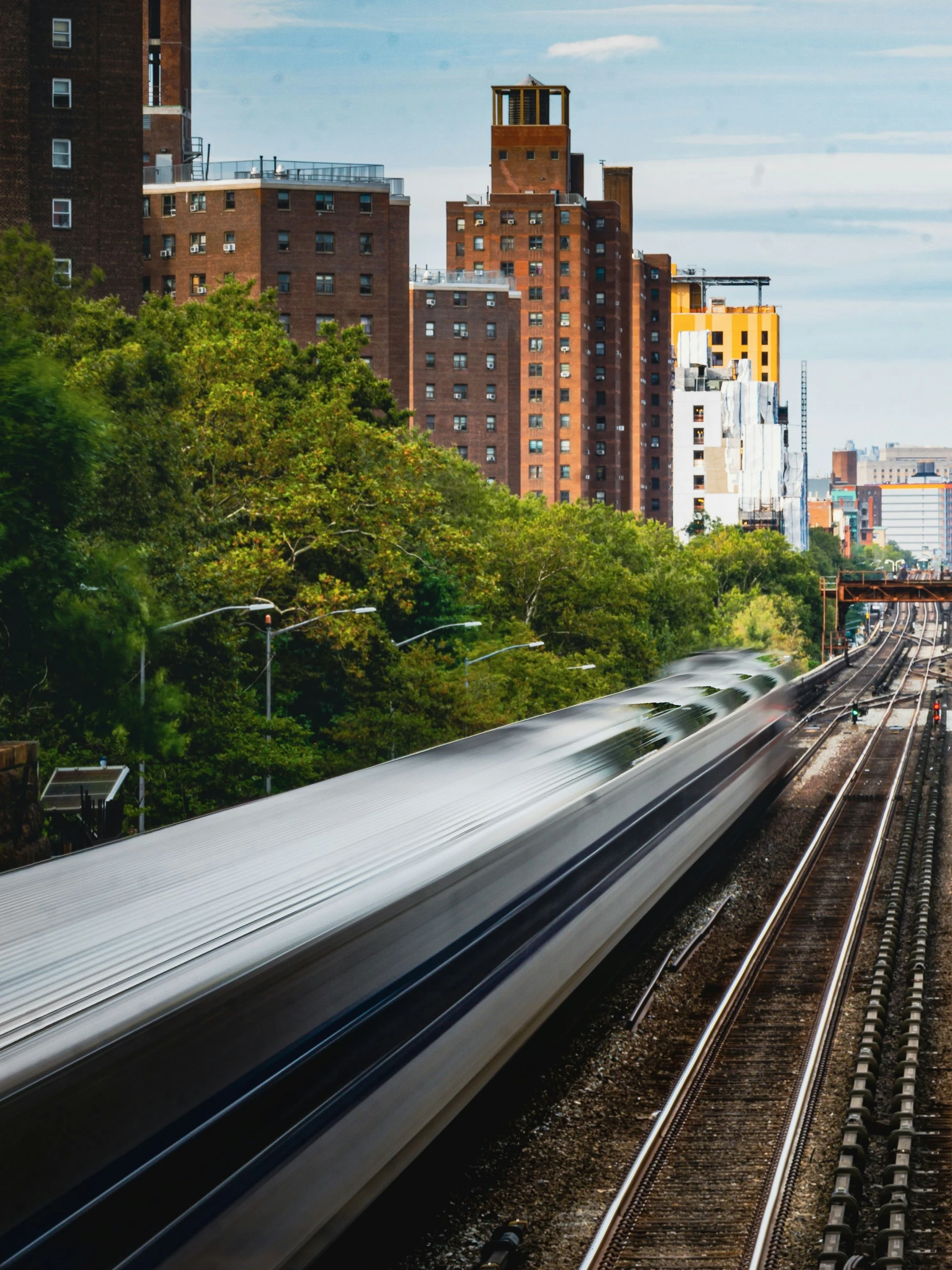 a silver train travels down the tracks near tall buildings