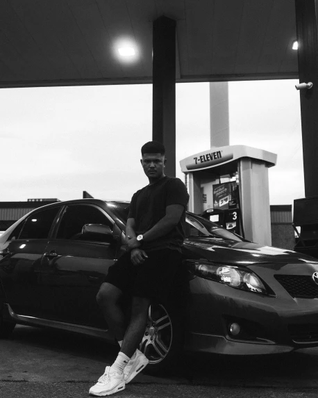 a man sitting on the hood of a car at a gas station