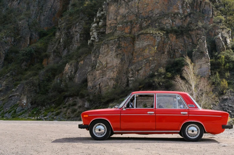 red old style car parked near rocky cliff