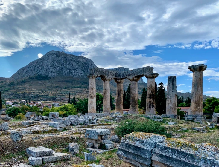 an ancient building and several pillars on a hill with a mountain in the background