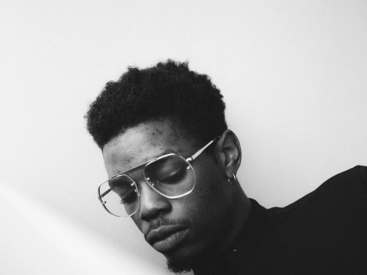 the young man is wearing sunglasses and sitting against a wall