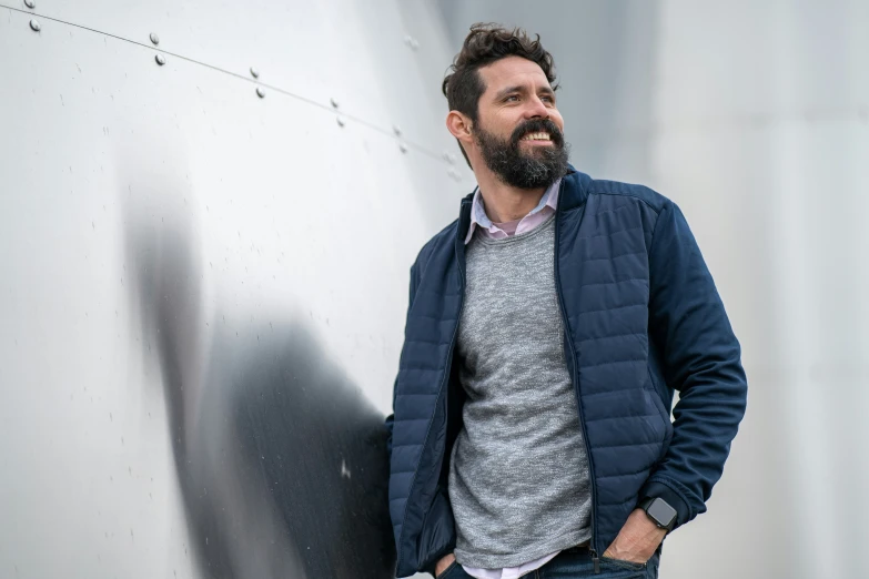 a man with beard leaning on the side of a building