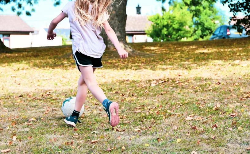 girl with blonde hair kicking a soccer ball on a field