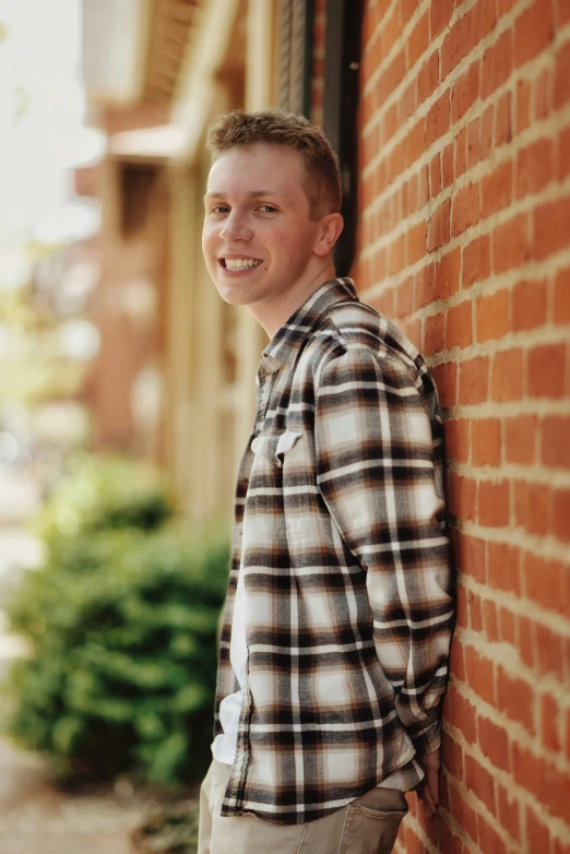 a man in a plaid shirt leans against the side of a building