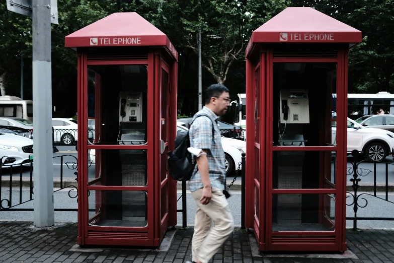 the man walks near some red phone booths