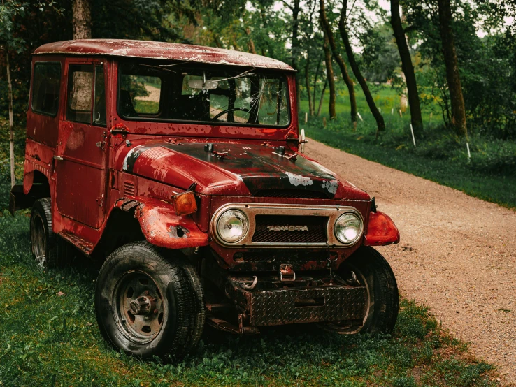 an old, rusty red car on a road in the woods