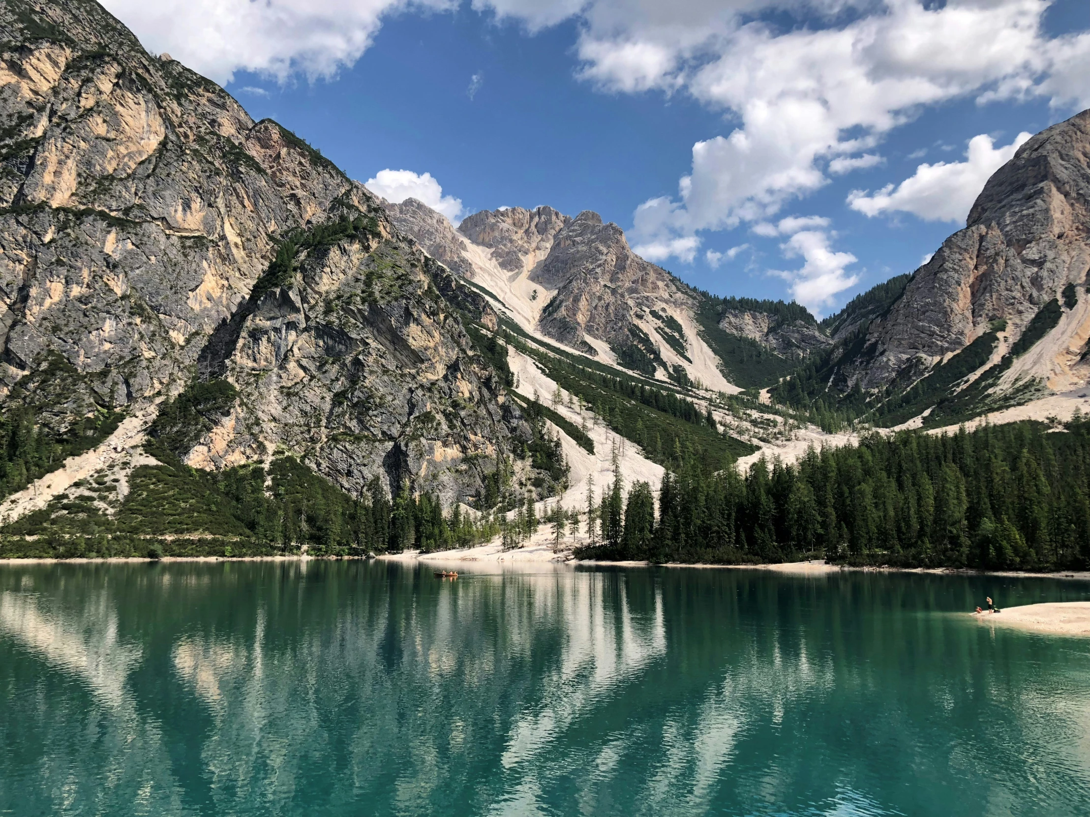 clear water surrounded by mountains and forest under a partly cloudy sky