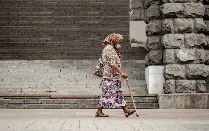 woman in floral dress walking past stairs with an old cane