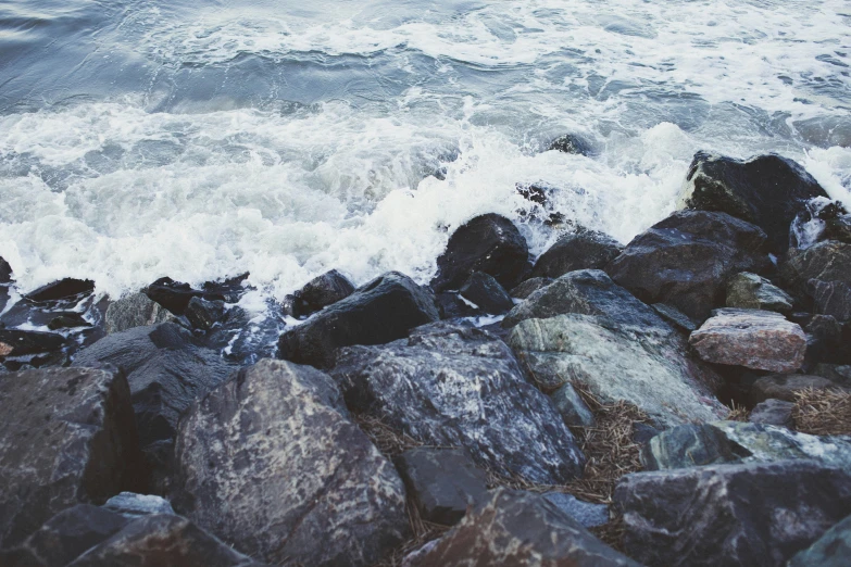 water crashing over rocks next to ocean in daylight