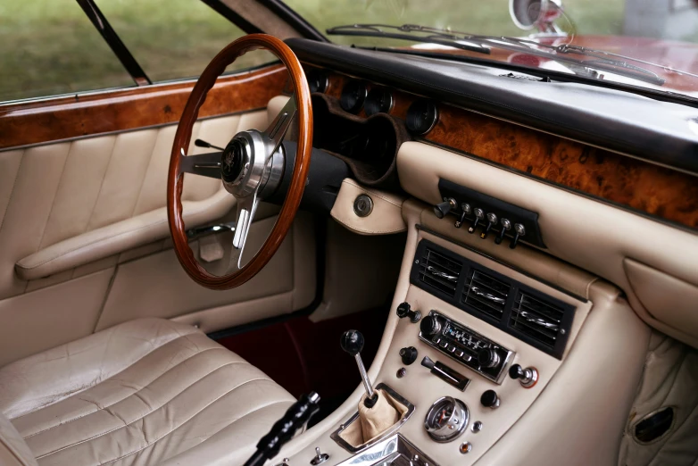 a dashboard view of a car that has a steering wheel, wood and beige leather