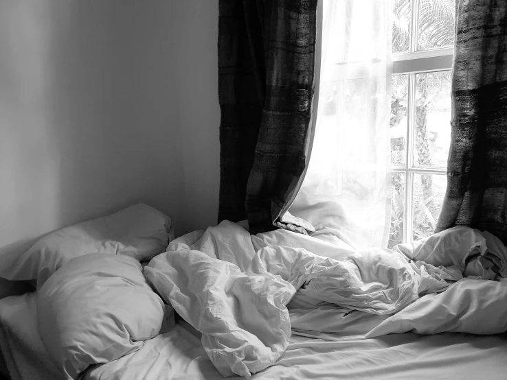 black and white pograph of an unmade bed near a window