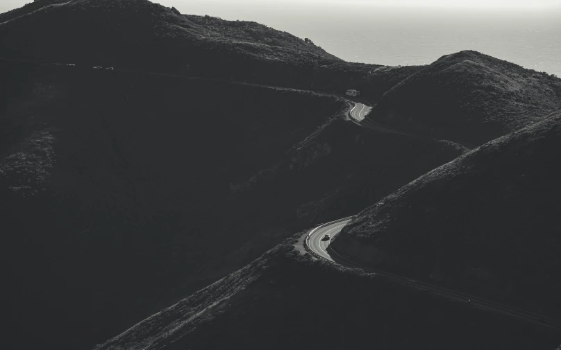 a long road going up a mountain with an ocean in the background