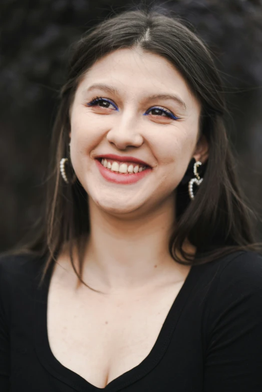 the young woman smiles wearing large earrings and a black top